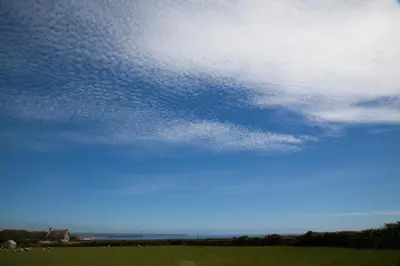 a cloudy sky over a green field with the ocean at Ewe With A View Sea View Shepherds Huts in Breage