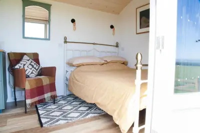 a bedroom with a bed and a chair at Ewe With A View Sea View Shepherds Huts in Breage