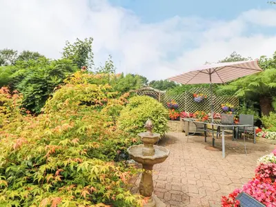a garden with a fountain and a table with an umbrella at The Hideaway in St Austell