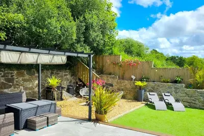 a garden with a stone wall and chairs and an umbrella at 4 Bed Villa Sleeps 8 -Private Terrace-Free parking in St Austell