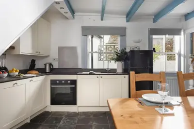 a kitchen with white cabinets and a wooden table at Saffron Cottage, St Ives in St Ives