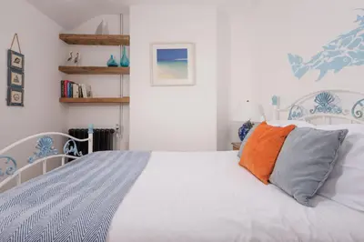 a bedroom with a white bed with an orange pillow at Saffron Cottage, St Ives in St Ives