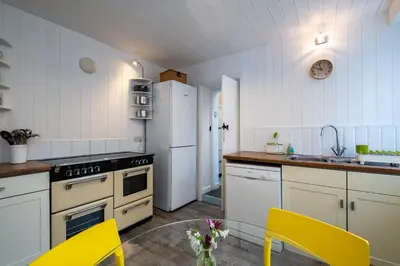 a kitchen with white appliances and a table and yellow chairs at Seapinks in Port Isaac
