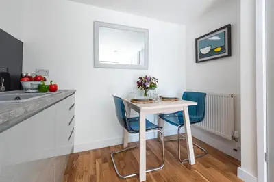 a kitchen with a white table and two blue chairs at The Studio, Rosebud. 5 minutes walk to beach. in Uny Lelant