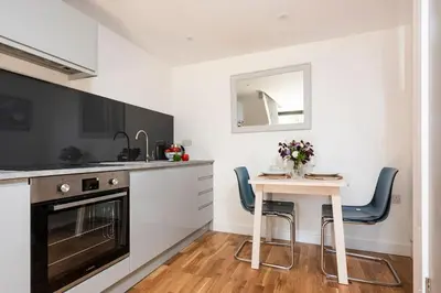 a kitchen with a small table and blue chairs at The Studio, Rosebud. 5 minutes walk to beach. in Uny Lelant