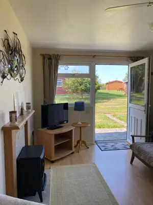 a living room with a tv and a sliding glass door at Chalet 86, Atlantic Bays Holiday Park in St Merryn