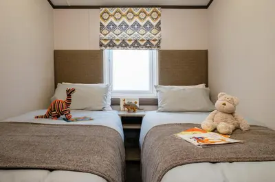 a teddy bear sitting on two beds in a room at Bailey Lodge in Padstow