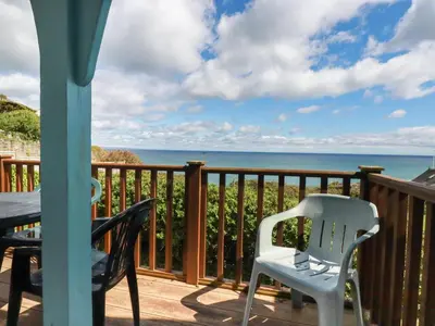a balcony with a table and chairs and the ocean at Beachcliff in Gorran Haven