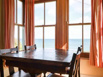 a dining room table with a view of the ocean at Beachcliff in Gorran Haven