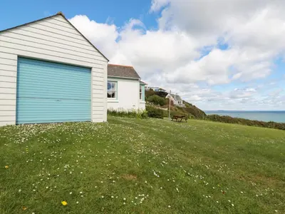 a white house with a blue garage next to the ocean at Beachcliff in Gorran Haven