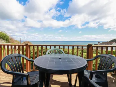 a table and chairs on a balcony with the ocean at Beachcliff in Gorran Haven