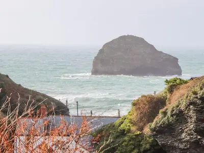 a view of a beach with a large rock in the ocean at Cliffside in Tintagel