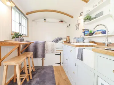 a kitchen with white cabinets and a wooden table at Gwithian Shepherds Hut in Hayle