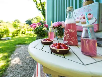 a table with two bottles of strawberry juice and a bowl of strawberries at Gwithian Shepherds Hut in Hayle